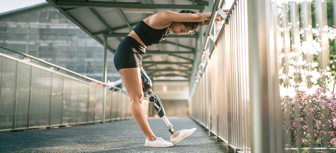 Braunhaarige junge Frau mit Beinprothese blickt auf den Boden, dehnt sich am Gelände
